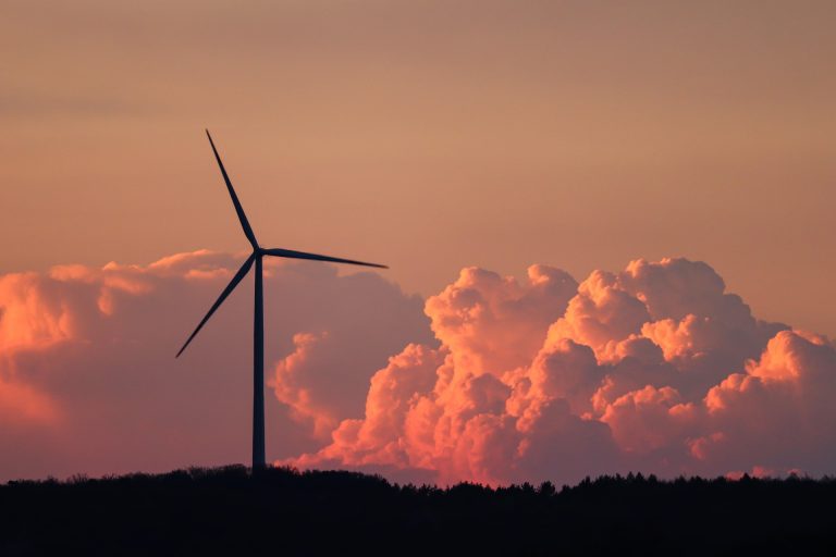 Tuulivoimalan taustalla pilviä oranssissa auringonpaisteessa.